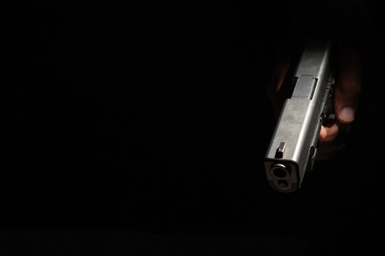 Close-up of a man's hand holding a small pistol ready to shoot in the dark, scary black background.defense or attack murderer or armed robber, First person view of a pistol.