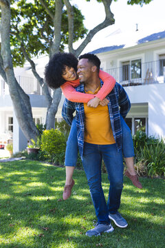 Happy african american couple riding piggyback in sunny garden, copy space