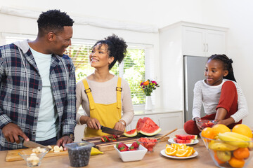 Happy african american family preparing fresh snack from fruits in kitchen at home, copy space
