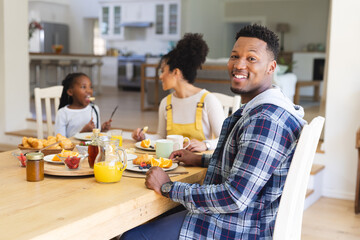 Happy african american man sitting at table, having a snack with family at home, copy space