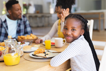 Happy african american girl sitting at table, having a snack with family at home, copy space