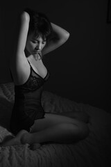 Black and white boudoir portrait of a young caucasian woman. She is wearing a night gown and is sitting in bed. The scene is dark. 
