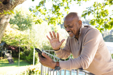 Naklejka na ściany i meble Happy african american senior man using smartphone on sunny terrace