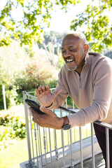 Happy african american senior man using smartphone on sunny terrace