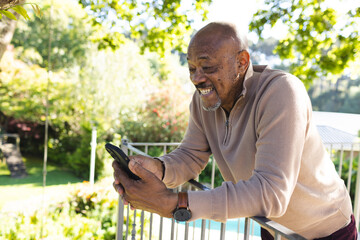Fototapeta premium Happy african american senior man using smartphone on sunny terrace