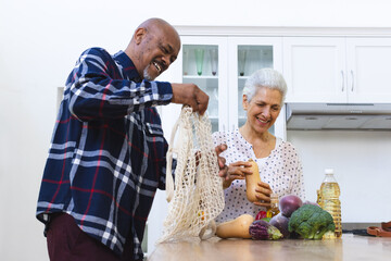 Happy diverse senior couple unpacking groceries in kitchen - Powered by Adobe