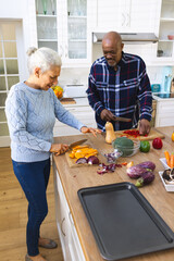 Diverse senior couple chopping vegetables in kitchen
