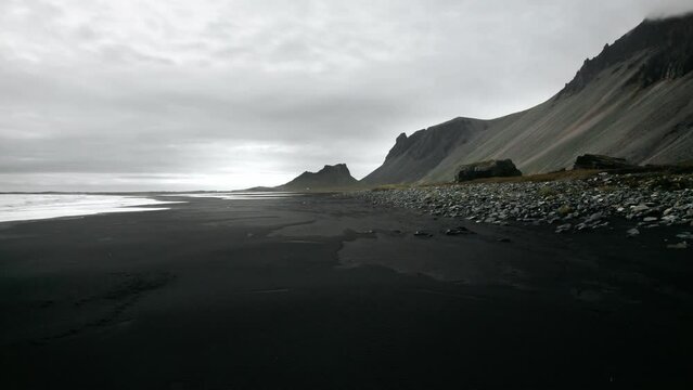 Flying through rock formation on black sand beach stokksnes, volcanic mountain landscape