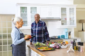Poster Diverse senior couple preparing meal using tablet in kitchen © wavebreak3