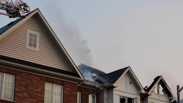 Fire fighters spray water as steam rises off of burnt charred house roof, static