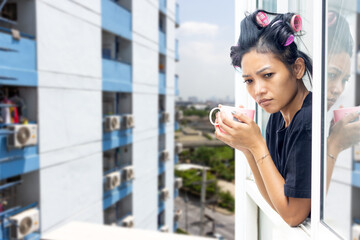A young woman in curlers looks out of the window of a high-rise building