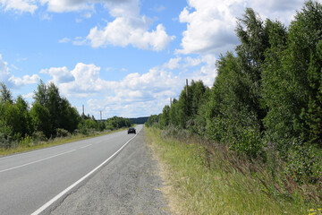 Fototapeta na wymiar Cars on the highway. Road along the forest. Beautiful summer landscape, white clouds on a blue sky.