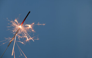 Sparkler burning on blue background, copy space for text.
