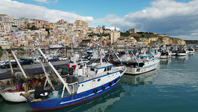 Drone flight past fishing boats and fishermen unloading boxes of freshly caught fish in Sciacca harbor, industry and scenery in Sicily Italy
