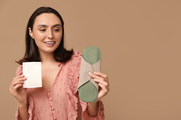 Beautiful young woman with reusable menstrual pad on brown background