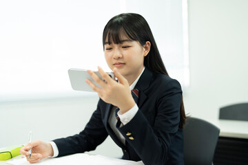 教室でスマートフォン使用している制服の高校生