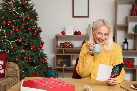 Mature woman with coffee cup reading greeting card for Christmas celebration at home