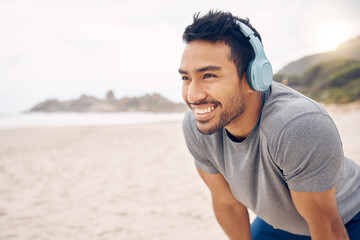 Break, beach and man workout to relax with a smile after cardio exercise. Fitness, jog and healthy athlete or male person rest in natural ocean with headphones for music and physical wellness - obrazy, fototapety, plakaty