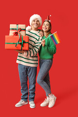 Young couple in Santa hats with LGBT flag and Christmas gifts on red background