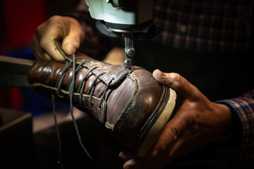 Schuster, der einen alten Schuh in den Händen hält und an der Nähmaschine reparieren will - obrazy, fototapety, plakaty