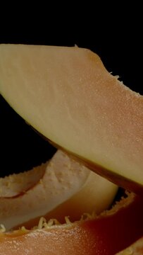 Vertical video. Sliced Seedless Papaya Wedges on a Black Background. Dolly slider extreme close-up.