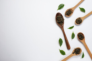 Dry green tea on a wooden spoons with a fresh gren leaves, isolated on white background. Top view, falt lay. Space for text, copy space. - obrazy, fototapety, plakaty