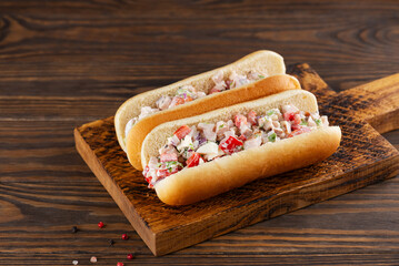 Chopped Italian sandwich with ham, cheese, sweet pepper, onion, lettuce and spices in hot dog buns in a wooden board.