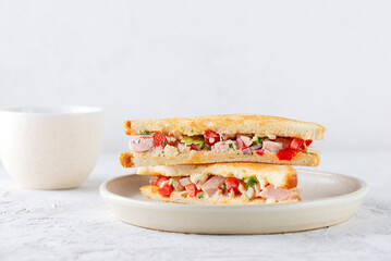 Chopped Italian sandwich with ham, cheese, sweet pepper, onion, lettuce and spices and cup of tea on a white table.