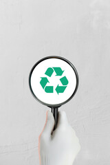 An employee's hand holds a magnifying glass for inspecting materials or trash for recycling.