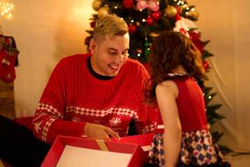 Obraz na płótnie Canvas young man opening a gift box with a little girl on Christmas day at home