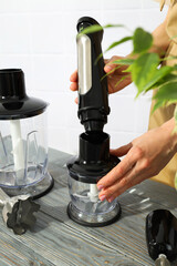 Black blender with attachments in hands on wooden table on white background