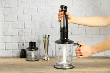 Black blender with attachments on wooden table and hands on light background