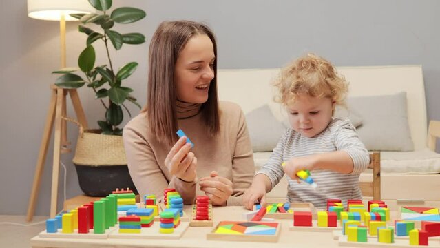 Sensory exploration. Attachment bonding. Patience resilience. Independent play. Cheerful Caucasian woman playing with her infant baby daughter in home interior.