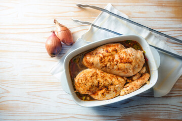 Meat dish from spicy chicken breast fillet with onions and vegetable broth in a casserole for the oven, cooking poultry at home, high angle view from above, copy space
