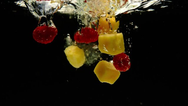 Super slow motion of fresh mango and pineapple falling into water on black background. Filmed on high speed cinema camera, 600 fps.