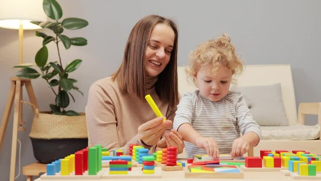 Motor skills. Geometric shapes. Rainbow toys. Shape sorter. Emotional intelligence. Young mother playing with her toddler baby daughter in home interior.