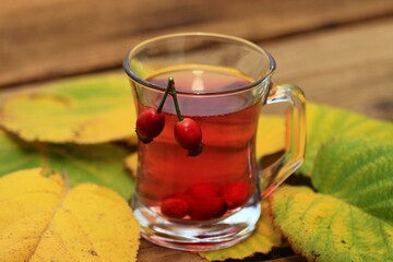 Rosehip tea tea full of vitamins on wood table. Autumn mood and colors come from fresh and   rosehips and november leaves.