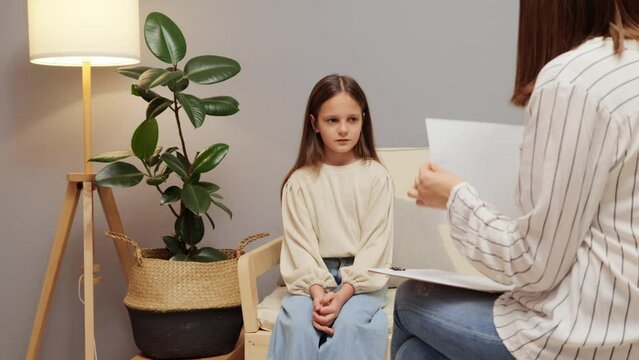 Kid's counseling session. Child's emotional comfort. School psychologist discussion. Therapist's empathy talk. Child psychologist showing picture to little smart girl doing psychological test.