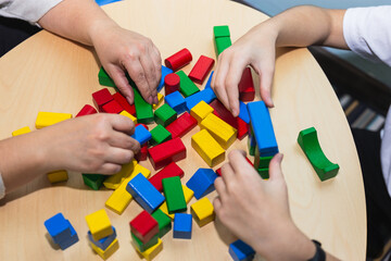 Top view of the hands of an adolescent patient and her psychotherapist working with colorful wooden toy blocks in therapy. Concept of therapy and mental health - obrazy, fototapety, plakaty