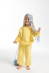 Pretty little girl in yellow clothes plays with ball of blue thread. Child model with long blond hair sits in studio on light background. High quality photo