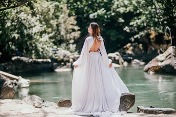 a beautiful woman in a long white dress looks into the distance at a beautiful lake with swans rear view