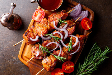 Pork kebab with barbecue sauce and tomatoes on a dark background, top view close up