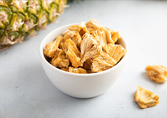 Dried pineapple slices chips in glass bowl on light background with ripe pineapple fruit.Macro