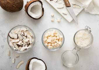 Sweet dried coconut flakes with bites and slices in glass jar with ripe coconuts on light table.Top  view.