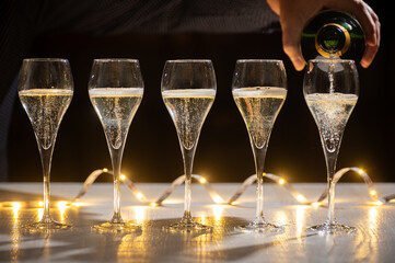 New year party, pouring of brut champagne bubbles cava or prosecco wine in tulip glasses with garland  lights on background - obrazy, fototapety, plakaty