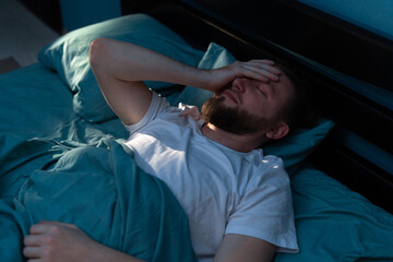 Depressed millennial tired man awake in the night touching his forehead and suffering from insomnia