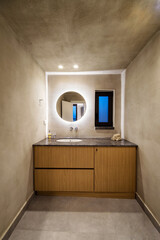 Luxury Grayish Bathroom: Wall-to-Wall Wooden Cabinet, Stylish Sink, and Backlit Round Mirror. refined interior design, this image is ideal for use in home decor publications. 