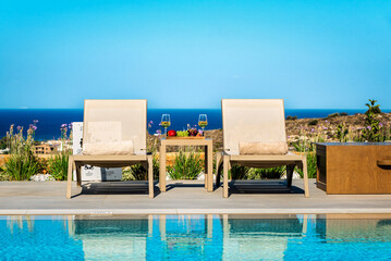 Sunny summer day by the pool, two sunbeds overlooking panoramic sea view. Selective focus.