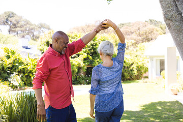 Happy diverse senior couple dancing in sunny garden
