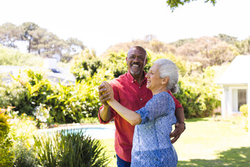 Happy diverse senior couple dancing in sunny garden